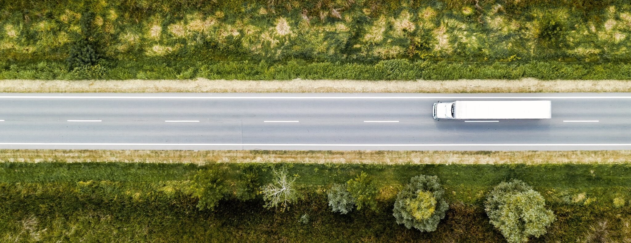A white truck on a straight road seen from directly above.